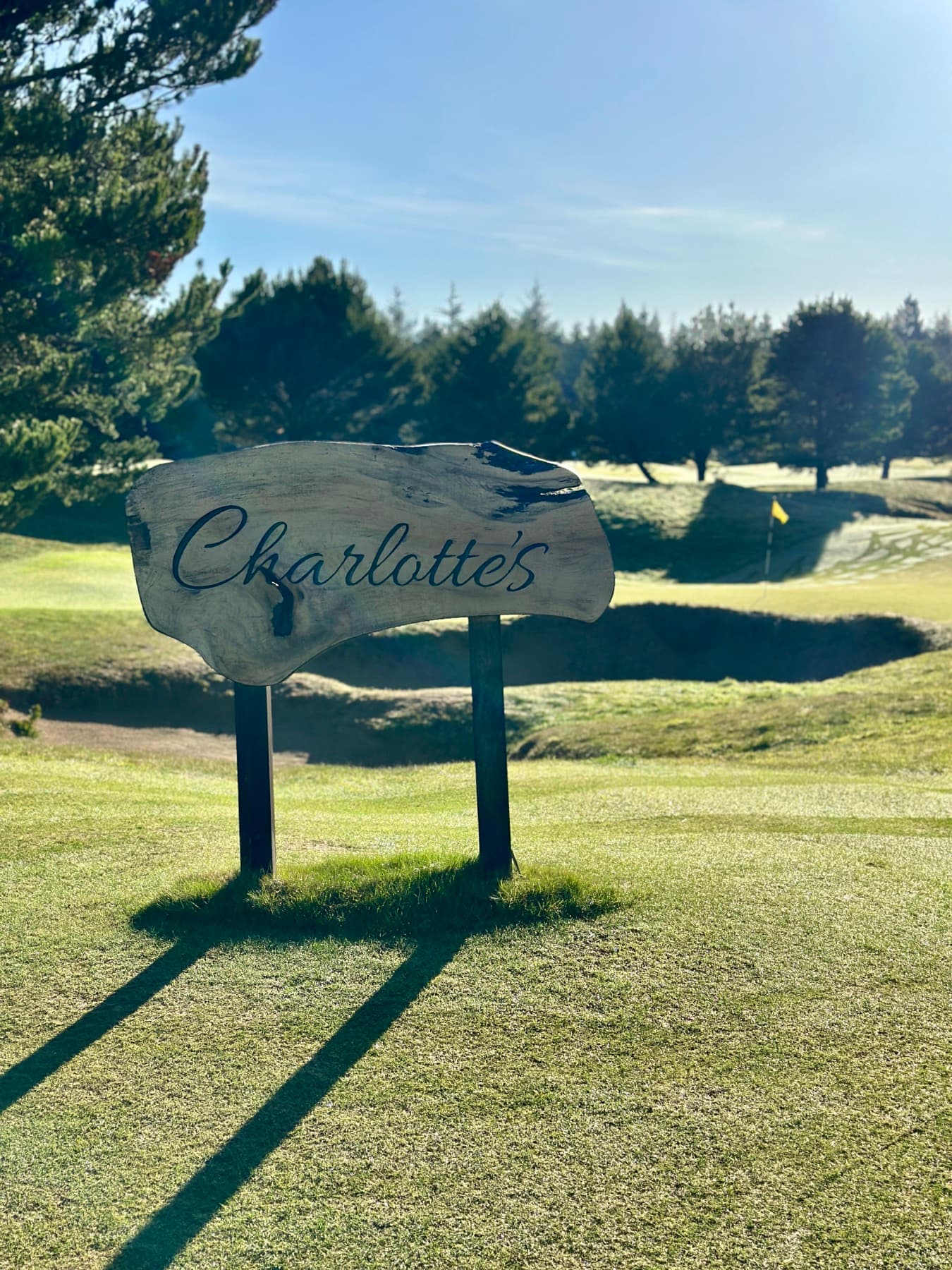 the hand-lettered 'Charlotte's' course sign, a par-3 green and dune bunkers beyond