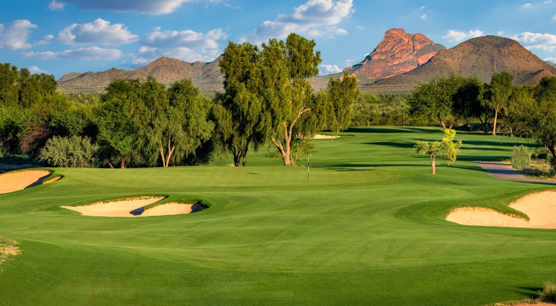a parkland green framed by trees, a red butte behind